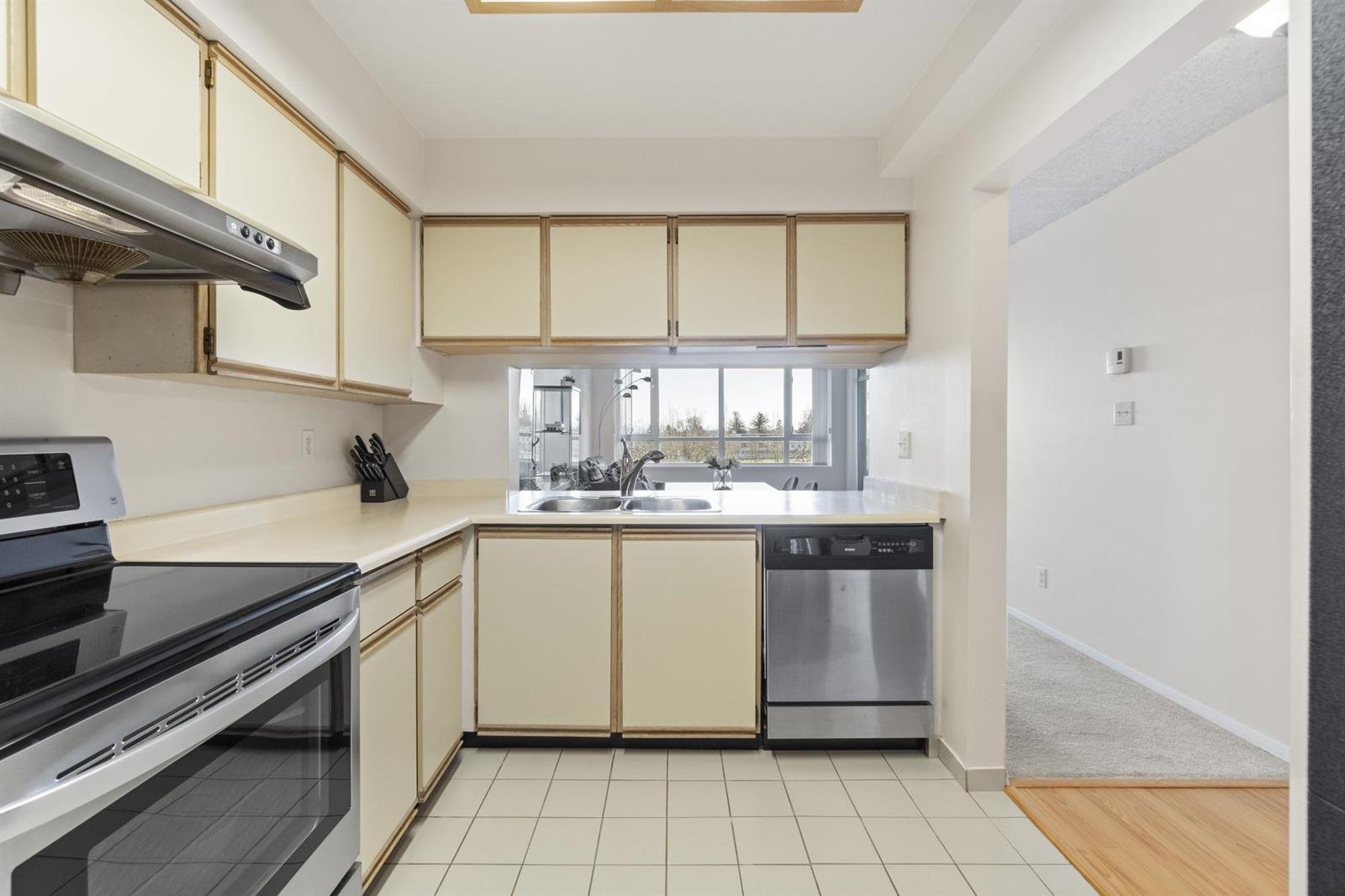 The kitchen from the doorway, the sink under a window with the dishwasher beside it.
