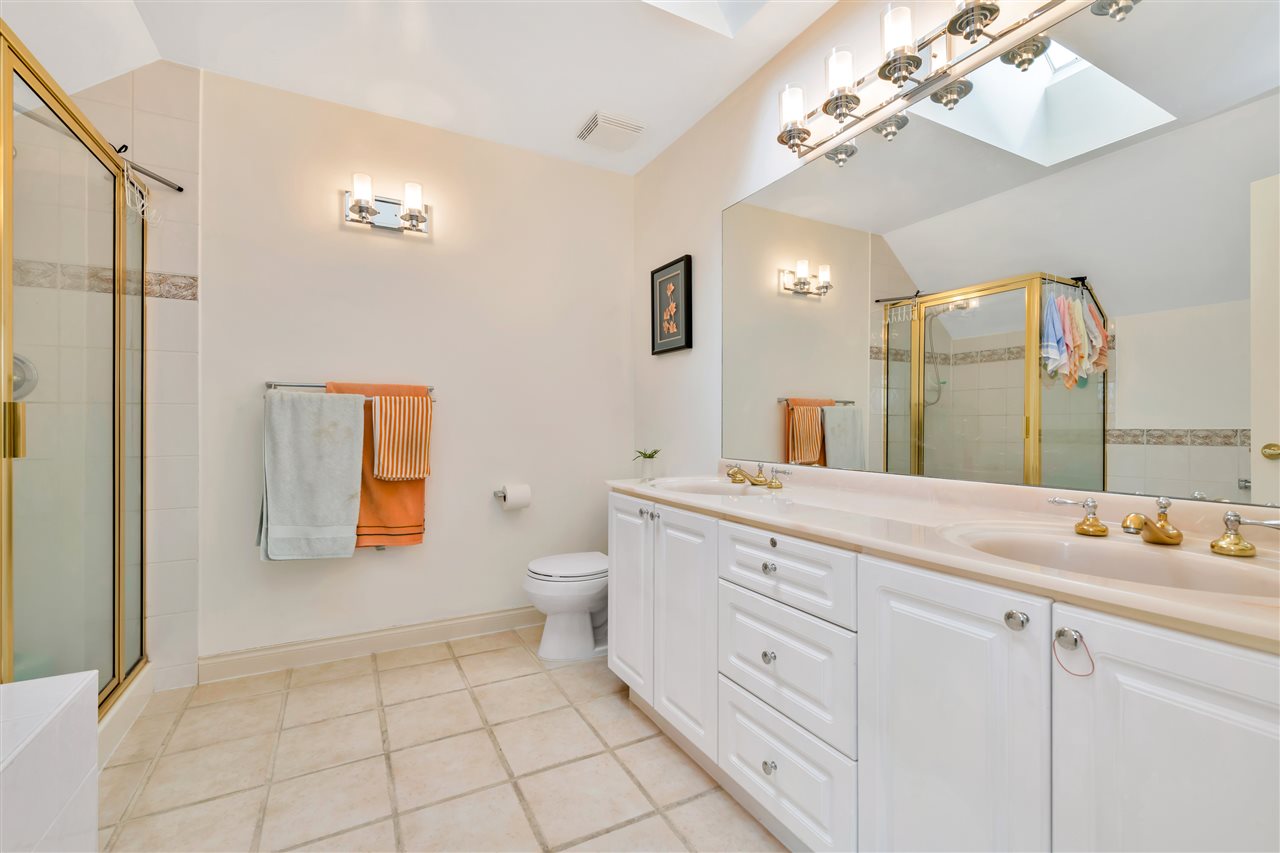 The ensuite, a glass shower beside the tub and a double vanity under a skylight.