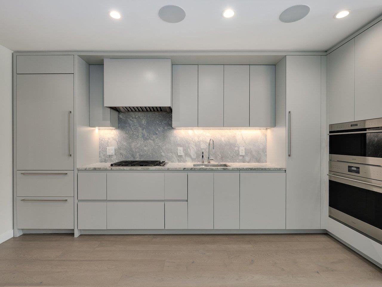 The kitchen wall in full: gas cooktop under a marble backsplash, wall oven and microwave to the right, refrigerator behind matching cabinet fronts.