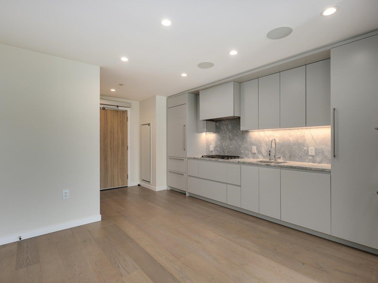 The kitchen seen down its length from the living area, with the timber entry door at the far end.