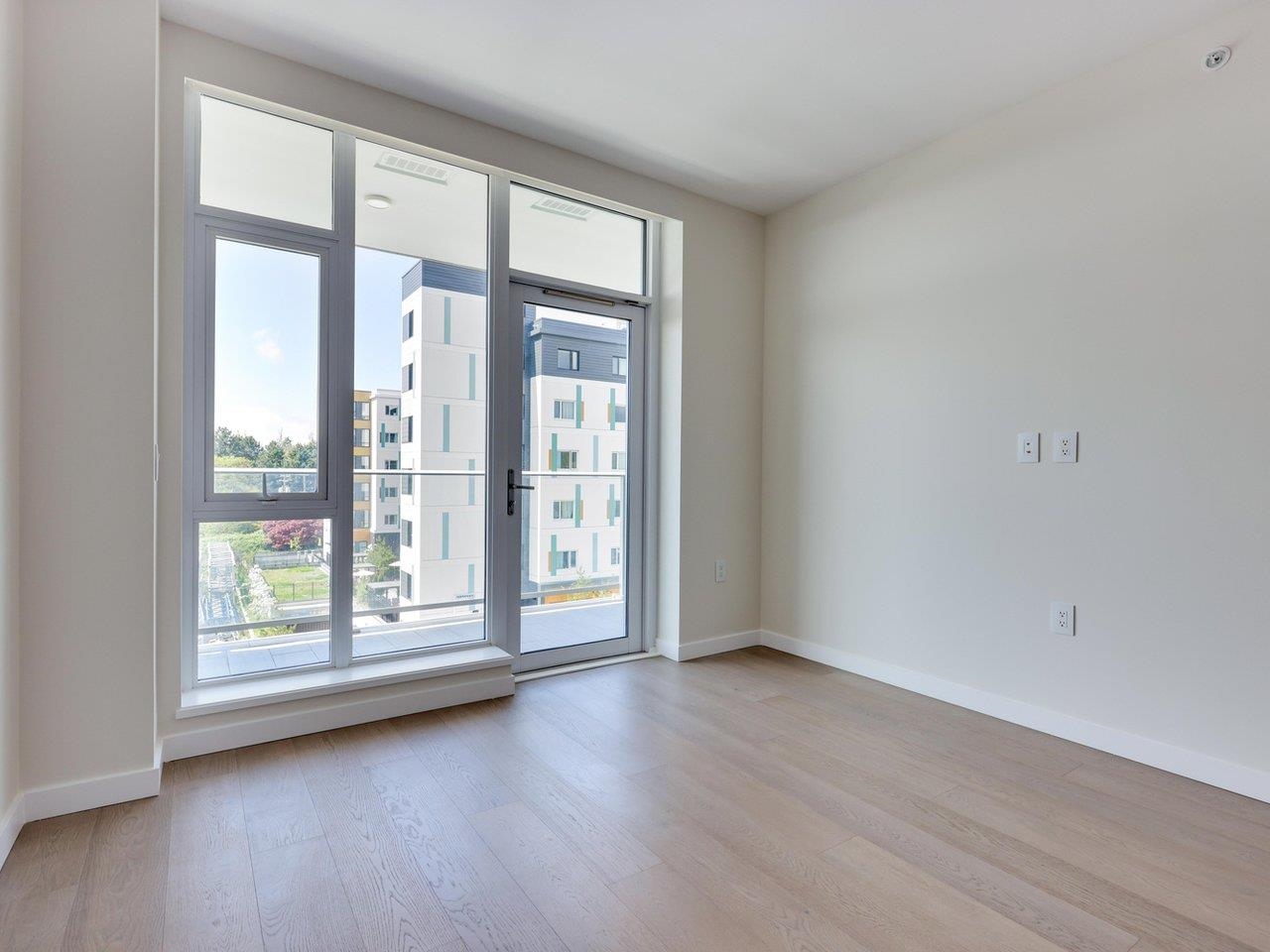The living room, empty, with a sliding glass door and full-height windows onto the balcony.