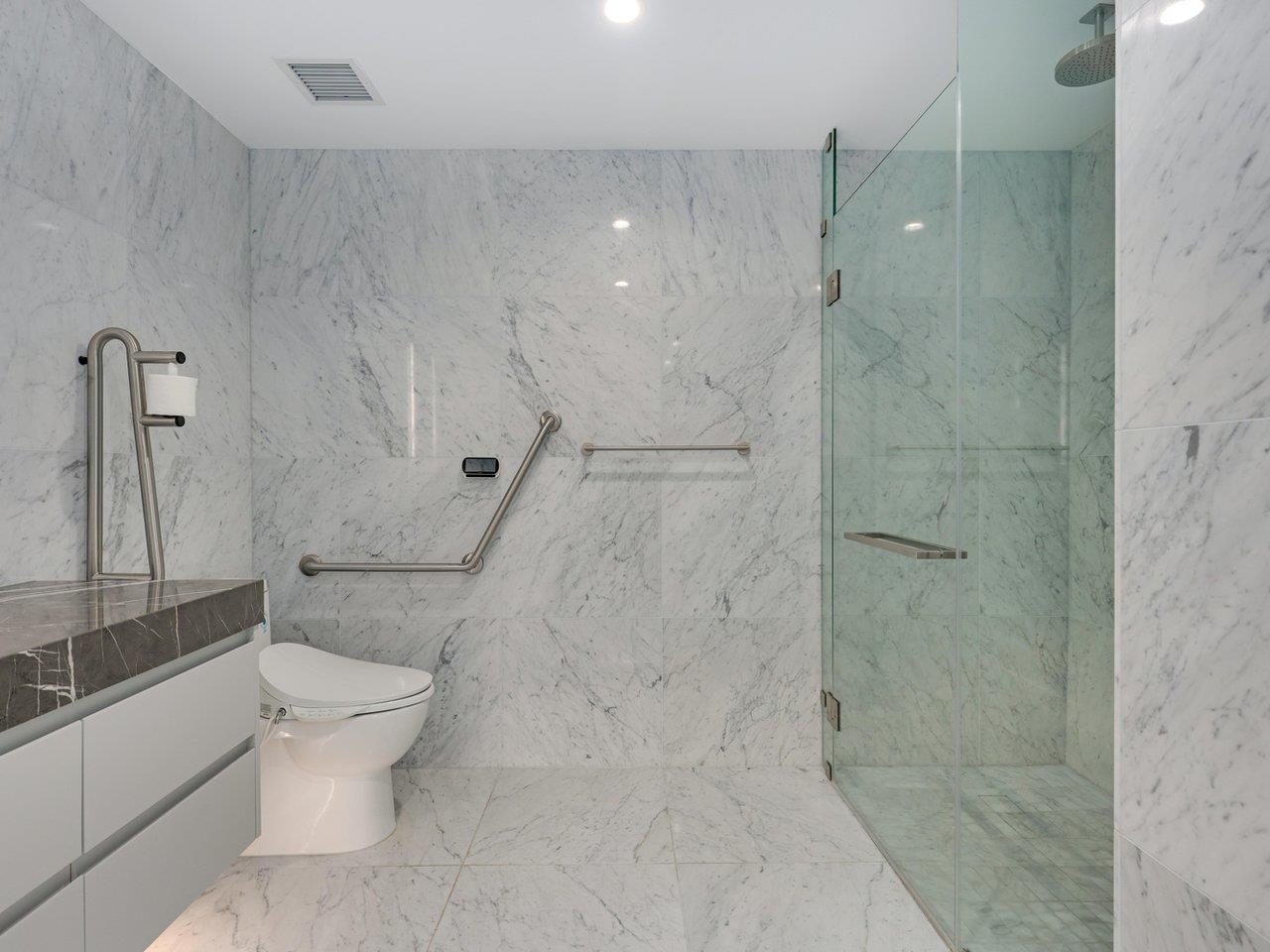 The walk-in shower, level with the floor and screened in clear glass, with a grab rail along the wall.