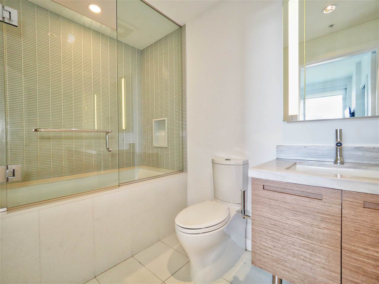The second bathroom, the tub and glass shower beside a vanity and mirror.