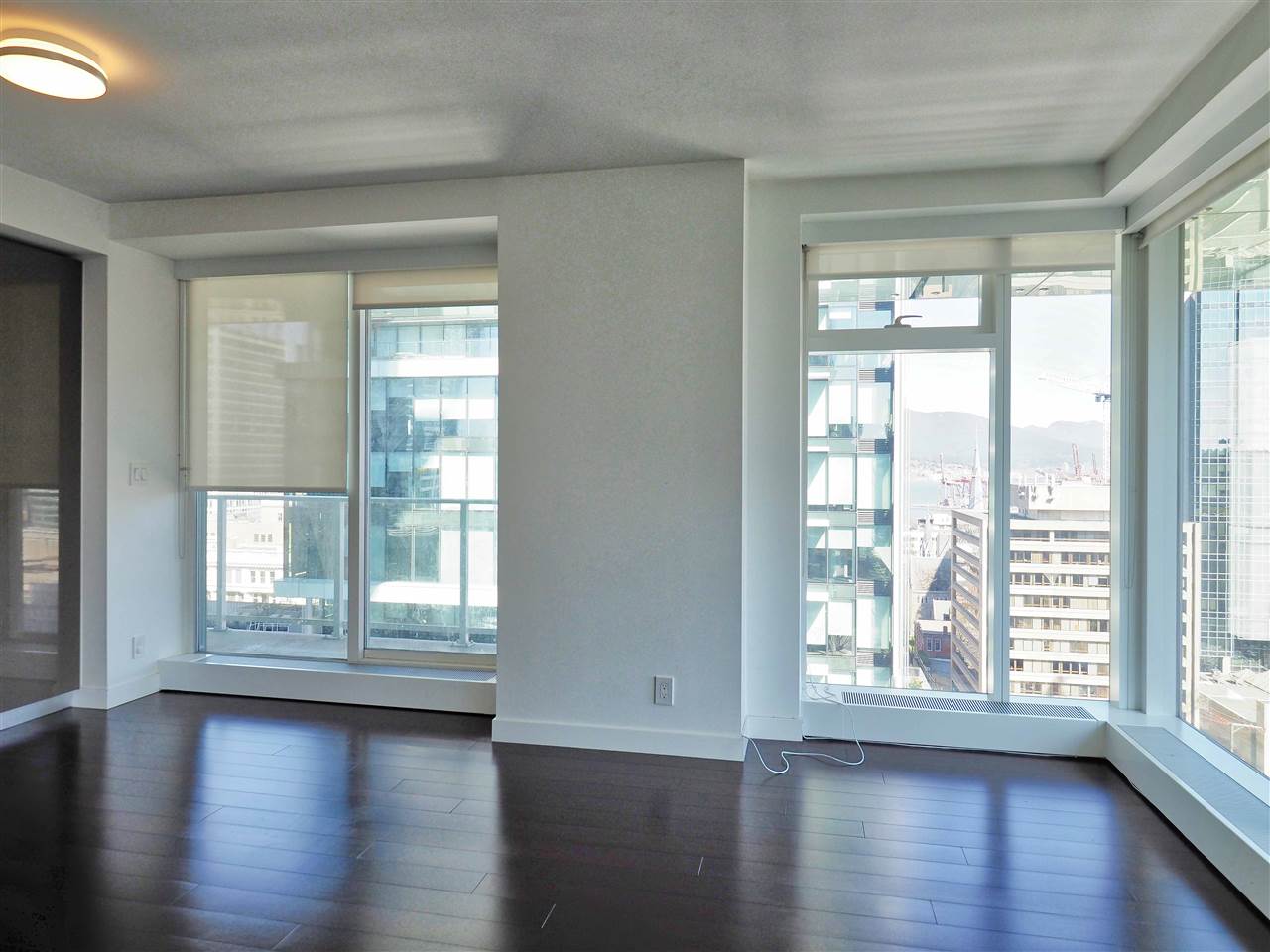 The living room toward the windows, dark hardwood running to the glass and the towers opposite.