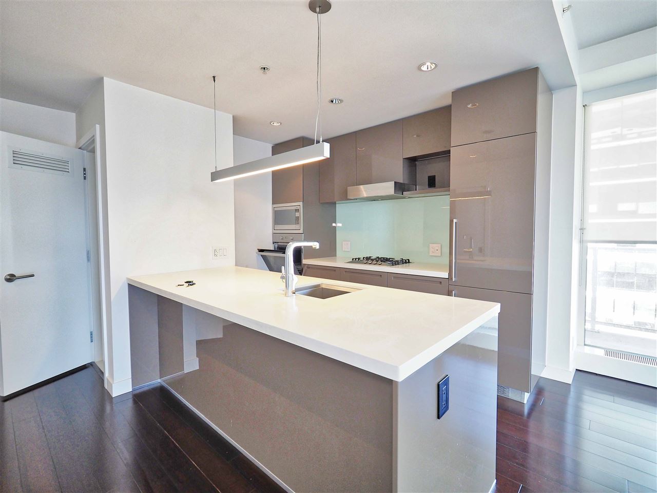 The kitchen island, a long quartz counter with the sink set into it and the pendant light above.