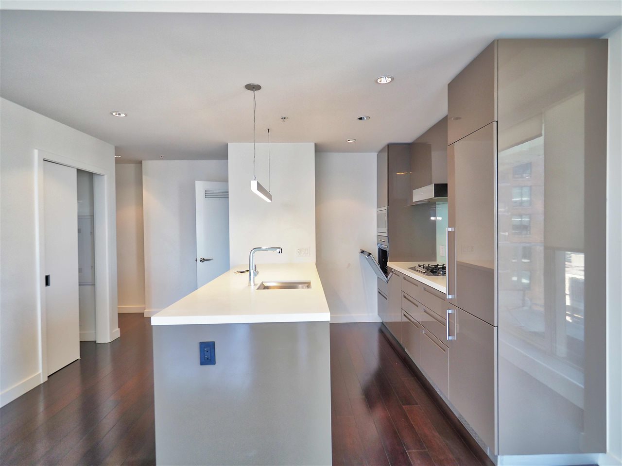 The kitchen along its length, the gloss cabinetry and the cooktop set into the island opposite.