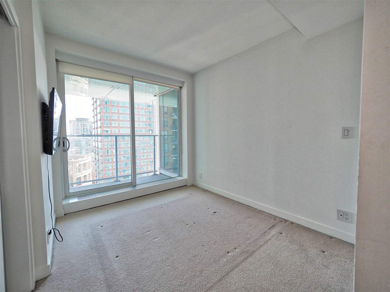 A bedroom, carpeted, with a sliding window onto the city.