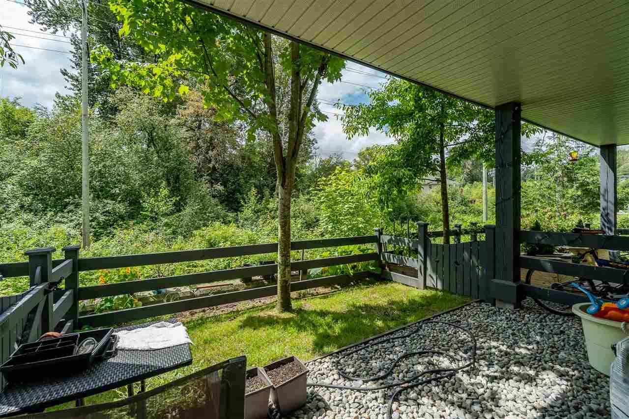 The yard from under the deck, a rail fence at the end of the grass and the greenbelt trees standing behind it.