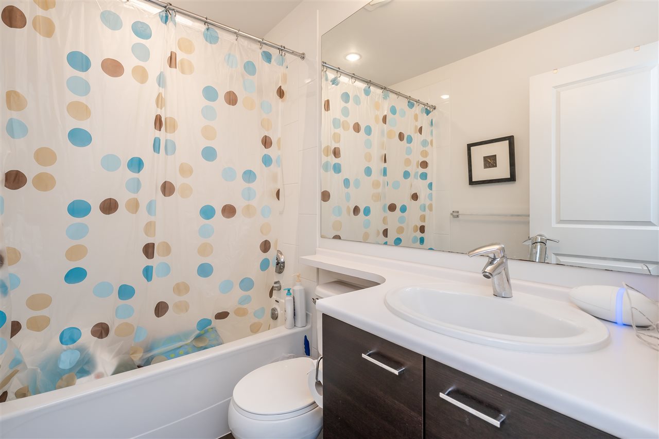 The second bathroom, a tub behind a patterned curtain with the vanity opposite.