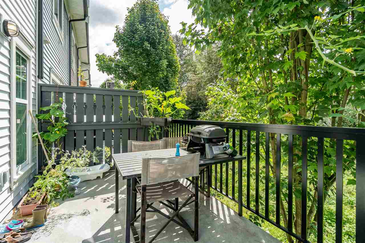 The deck, a barbecue and table with the trees close behind the rail.