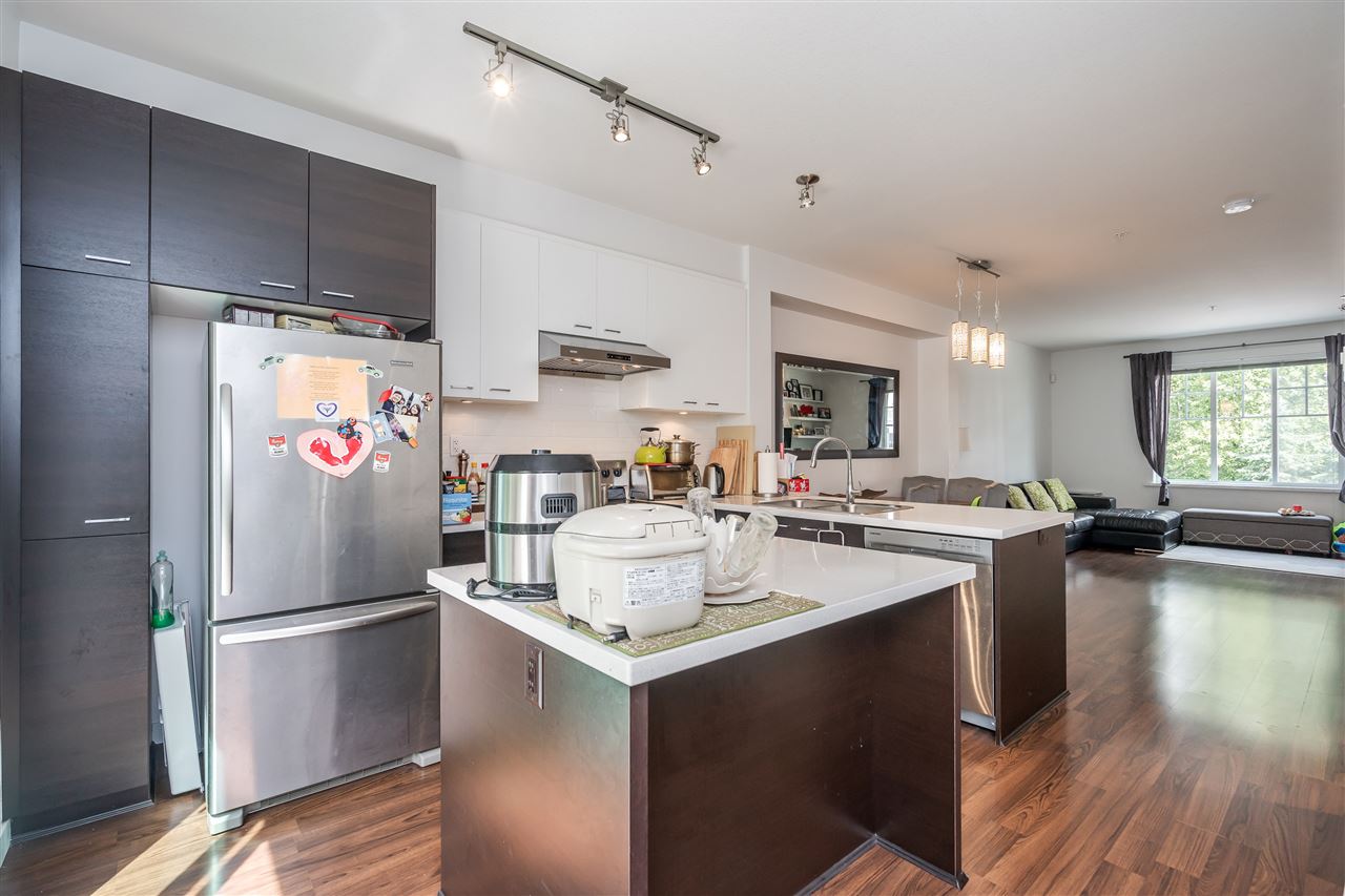 The kitchen, a stainless refrigerator beside the island with the living space running away behind it.