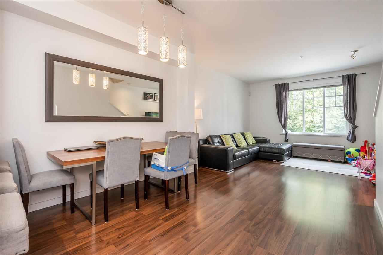 The living and dining rooms together, a sofa under the window and hardwood running the length.