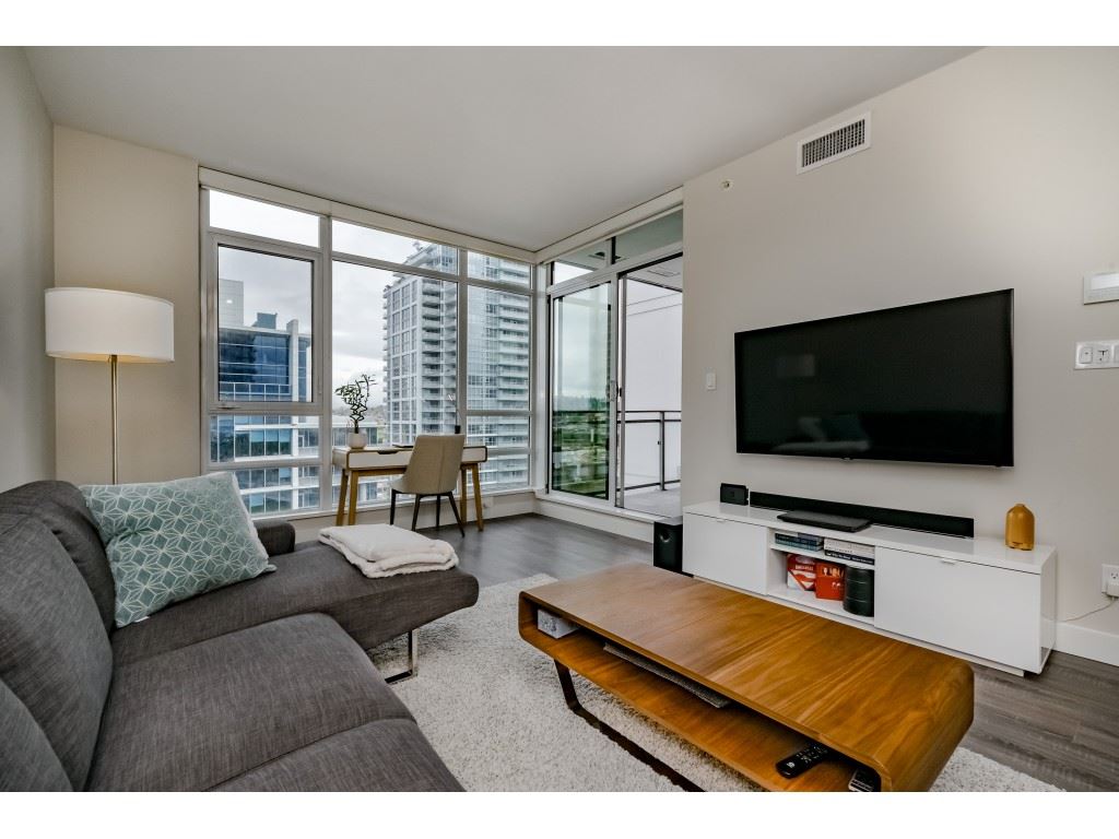 The living room from the window end, the television on the wall and the balcony door open at the side.