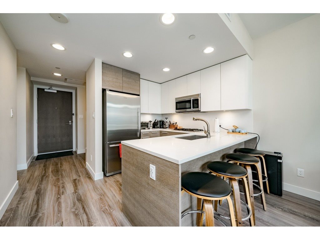 The kitchen island with three stools, the entry door and the tall fridge at the far end.