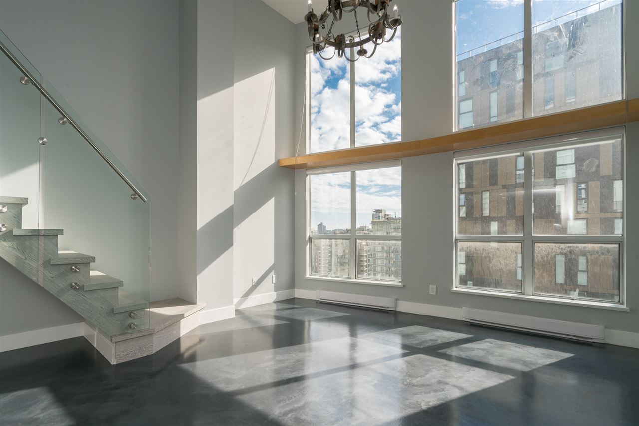 The living room under the double-height window wall, a chandelier hanging in the glass with the city beyond.