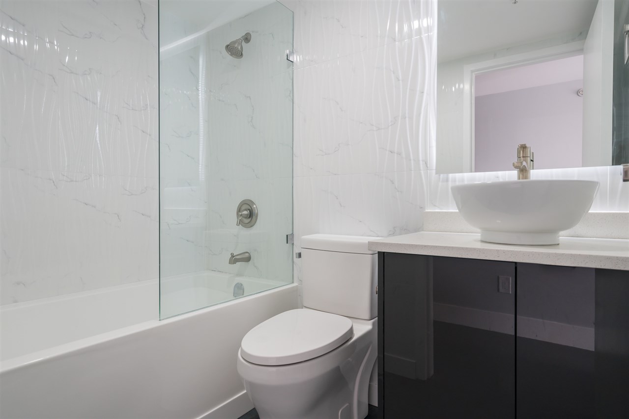 The bathroom, marble tile around the tub and a vessel basin on a dark vanity.