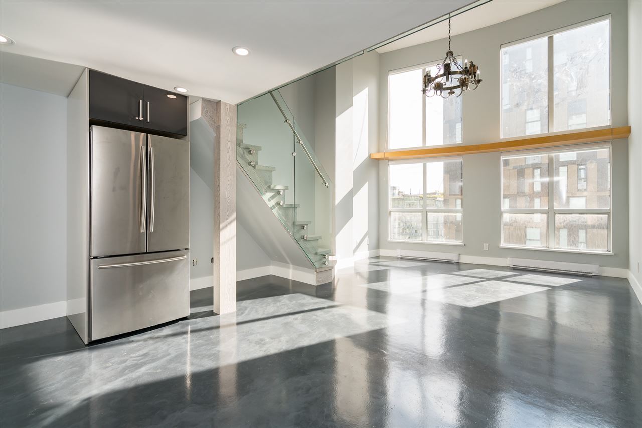 The kitchen and living room together, the stainless fridge at one end and the glass-railed stair rising to the loft.