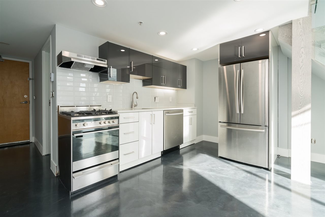 The kitchen along its wall, gas range and stainless appliances beneath the dark upper cabinets.