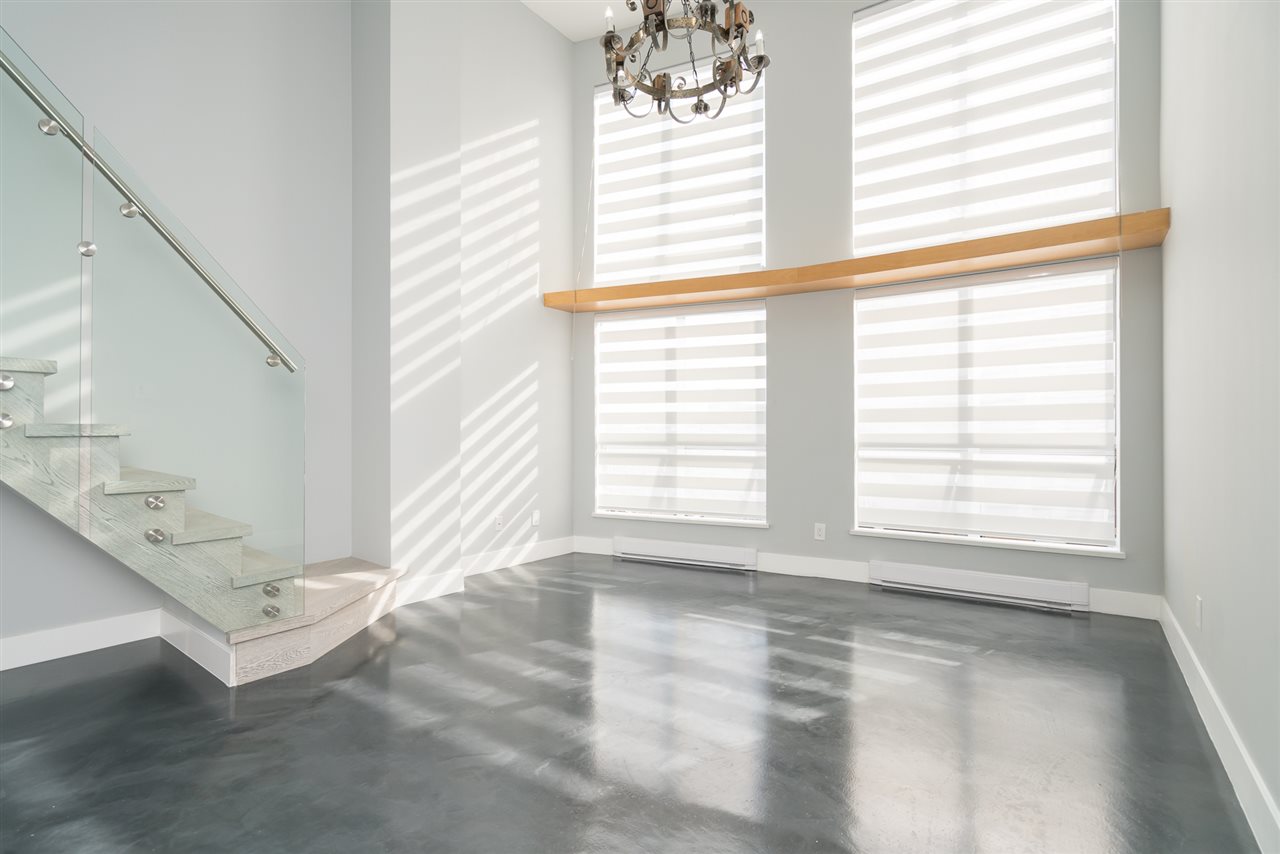 The staircase and its glass rail beside the tall windows, polished concrete underfoot.