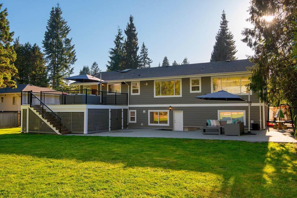 The back of the house across the lawn at dusk, cedars behind it and the deck lit up.