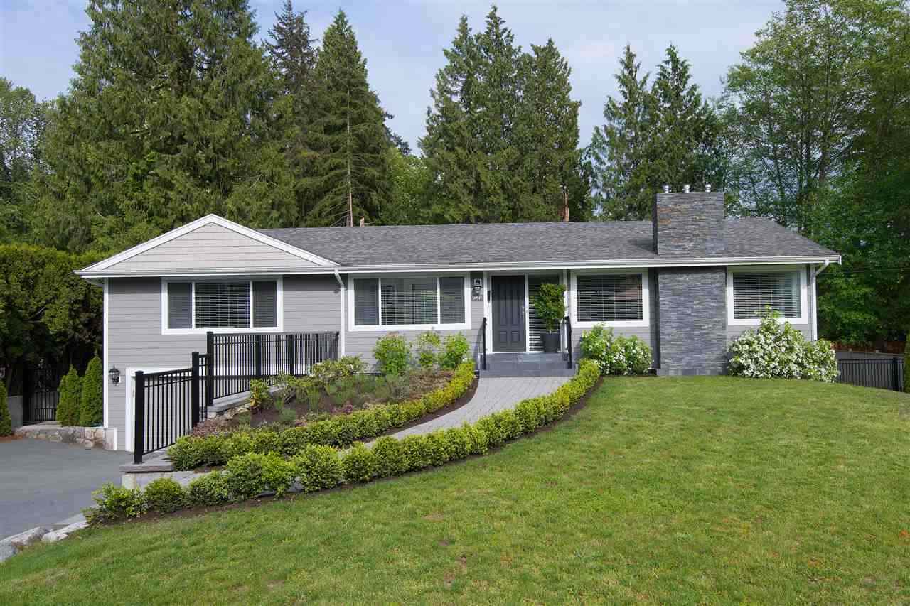 The front of the house from the street, low and grey behind a clipped hedge and a sloping lawn.