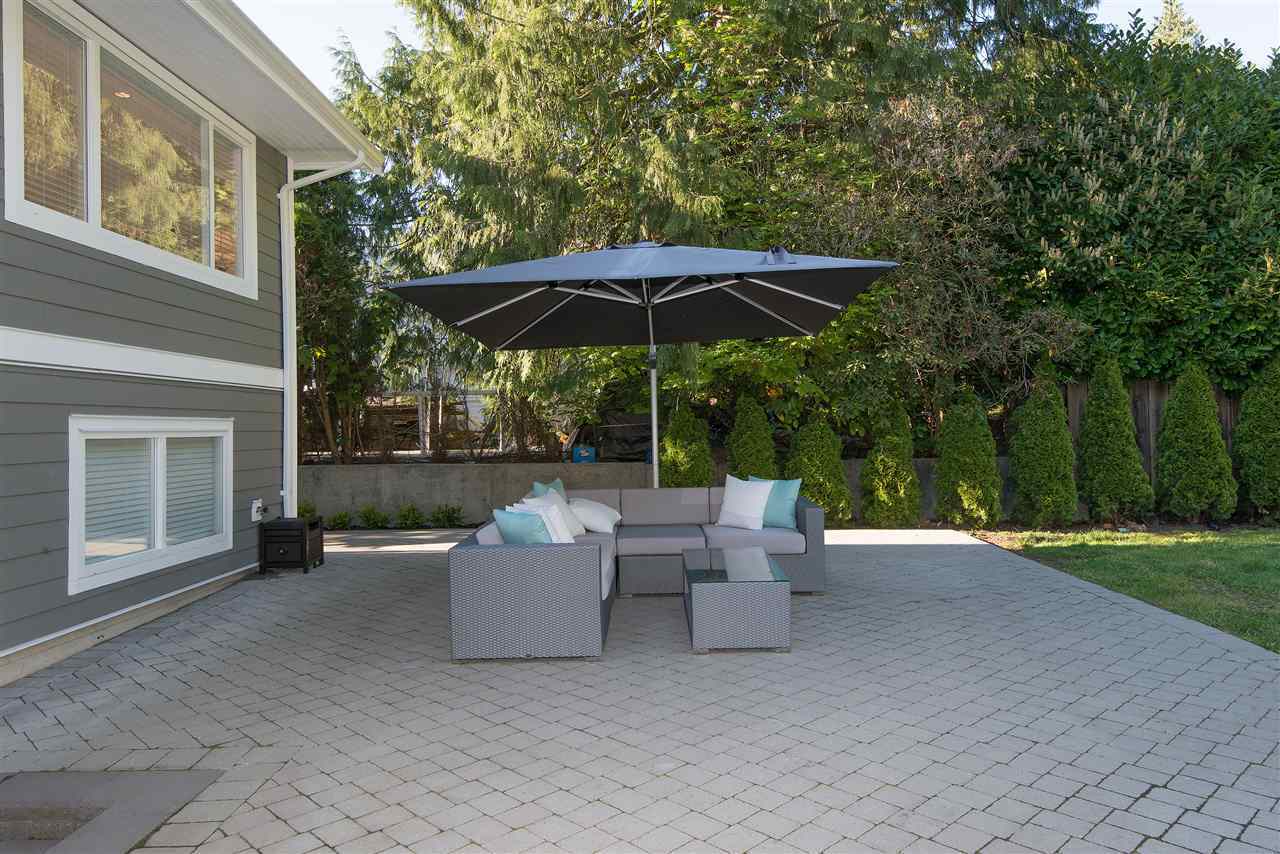 The patio beside the house, seating under an umbrella on grey pavers.