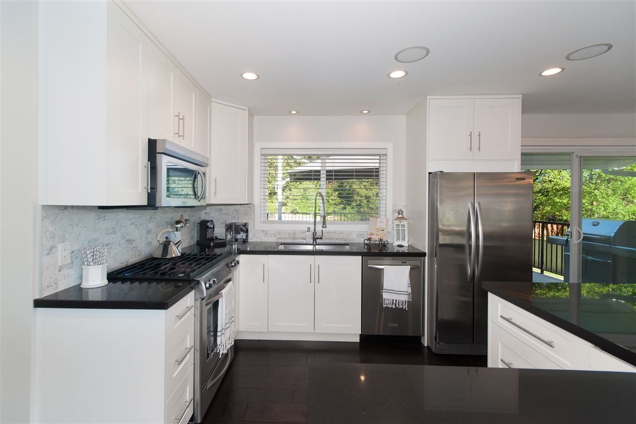 The kitchen, dark stone counters and stainless steel under white cabinets, a window over the sink.