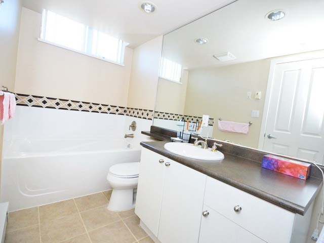The main bathroom, a tub along the tiled wall with the vanity beside it.