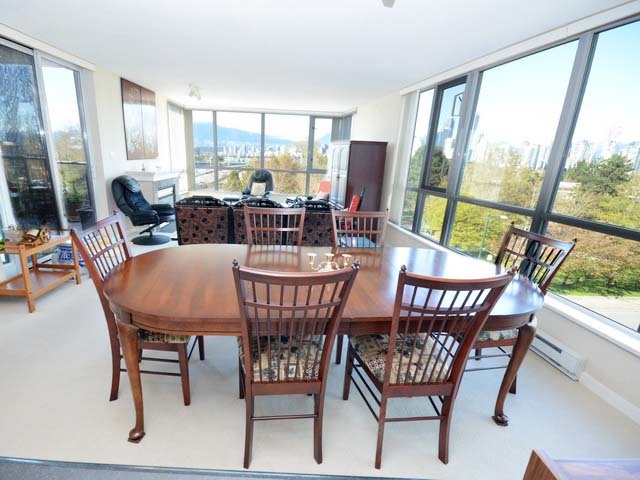The dining table under the corner windows, the park and the water filling the glass behind it.