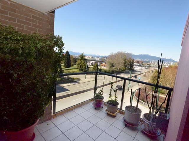 The covered balcony, potted plants along the rail, looking over the trees to False Creek and the mountains behind.